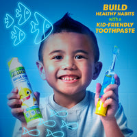 Child holding Baby Shark Light and Sound toothbrush and Firefly Kids Baby Shark Anti-Cavity Natural Fluoride Toothpaste, Bubble Gum Flavor. Build healthy habits with kid-friendly toothpaste